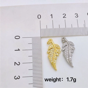 Gold and silver feather pendants with cubic zirconia accents measured on a scale