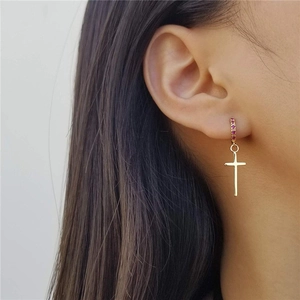 Close-up of gold cross pendant earrings with micro-set red cubic zirconia gemstones