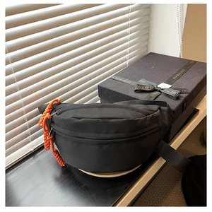 Detail of black canvas chest bag with orange woven rope zipper pulls near a gift box