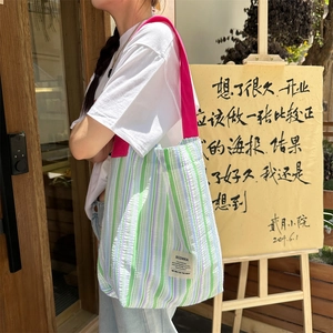 Détail du cabas en toile rayée avec bandoulière rouge et étiquette de marque latérale