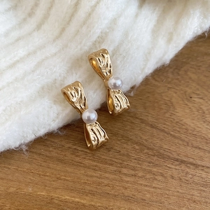 Dettaglio di orecchini a fiocco dorato plissettato con perla su maglia e sfondo di legno
