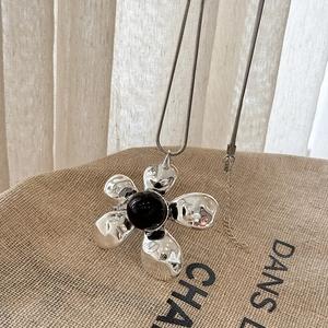 Detail of silver flower pendant with black bead on snake chain over linen texture