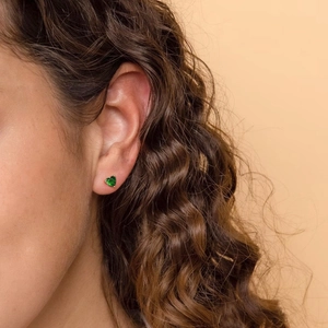 Elegant s925 silver heart stud earrings with green zircon on model in warm studio lighting