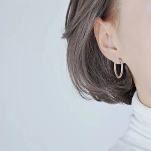Close-up of titanium steel hoop earrings with woven texture on a female model