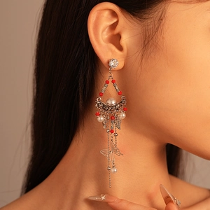 Detail of silver leaf earrings with red beads, pearls, and a butterfly tassel on a model