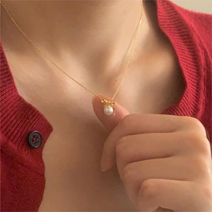 Close-up of gold bow necklace with pearl pendant on a model wearing a red sweater