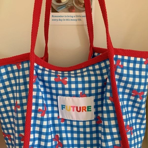 Detail of blue checkered tote bag with red bow pattern and Future rainbow embroidery