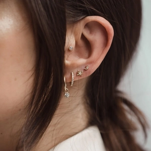 Close-up of woman wearing gold star, moon, and rhinestone stud earrings set in 925 silver