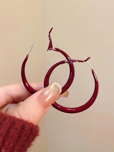Macro detail of deep red hoop earrings with high-gloss finish and silver needles