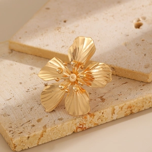 Détail d'une bague fleur dorée aux pétales texturés posée sur un support en pierre