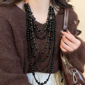 Detail of layered black beaded necklace with vintage tassels on a brown sweater