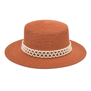 Detailed view of rust-red straw hat with intricate white pearl woven decorative band