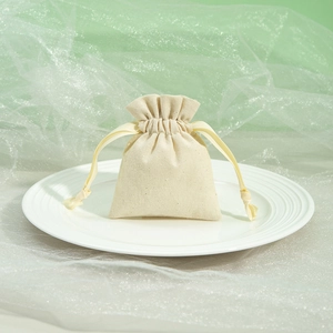 Close-up of a plain beige canvas drawstring jewelry pouch on a white plate background