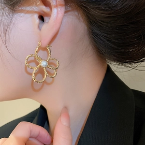 Detail of woven texture golden flower earring with pearl center worn by a model