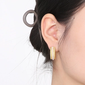 Close-up of gold C-shaped stainless steel earrings with woven texture and white pearls