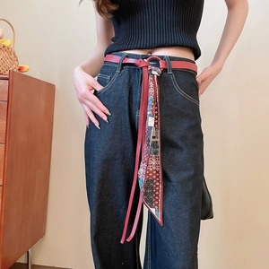 Detail of red leather belt with geometric print silk scarf tied on blue denim jeans