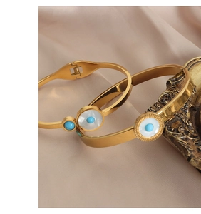 Detail of gold evil eye bangles with white shell and blue beads on silk fabric