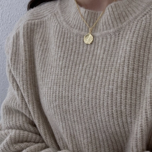Detailed view of irregular golden wave pendant necklace styled on a knit sweater