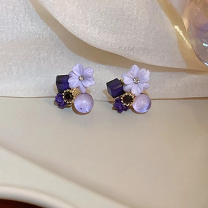 Detail view of purple resin flower earrings with amethyst beads on soft beige fabric