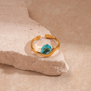 Détail de la bague dorée ondulée avec pierre bleu clair en forme de poire sur roche
