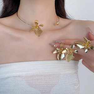 Detailed close-up of gold metallic flower jewelry set including collar necklace, earrings and ring