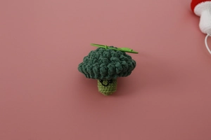 Detail of handmade crochet broccoli keychain with a smiling face on pink background