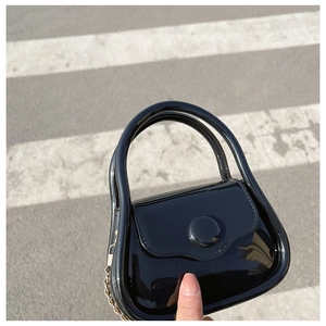 Close-up of mini black glossy chain bag held against a zebra crossing background