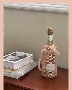 Detail view of pink beaded wine bottle bag with dual circular handles on wooden table