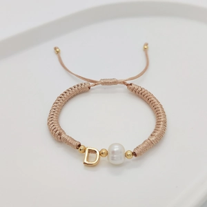 Detail of woven champagne cord bracelet with pearl and golden letter D charm