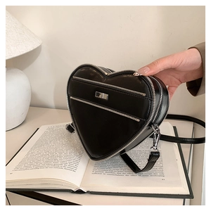 Detail of black heart-shaped handbag with silver zippers and adjustable strap on a book