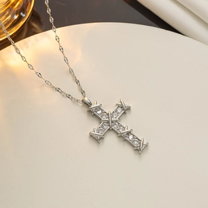 Close-up of silver cross necklace with inlaid clear cubic zirconia on a beige textured surface