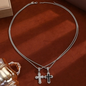 Detail of layered silver necklaces featuring two crystal-encrusted cross pendants on dark fabric
