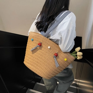 Handwoven straw tote bag with colorful pom poms and striped shoulder straps for beach trips