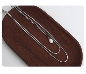 Close-up of double-layer silver titanium necklace with a baroque pearl on a wood tray