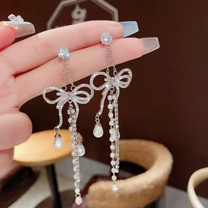 Elegant silver bow earrings with long diamond tassels and pearls shown on hand