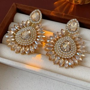 Detailed view of luxury gold sunflower earrings with pear-shaped crystals in a velvet box