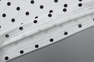 Detailed macro shot of fine stitching and black polka dots on white knit fabric