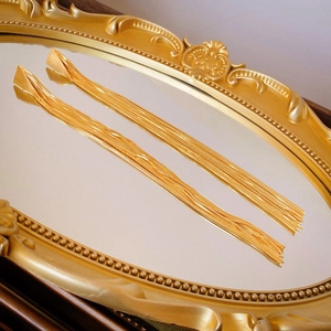 Close-up of golden geometric tassel earrings with sleek snake chains on vintage mirror