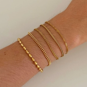 Close-up of five layered gold-plated stainless steel bracelets with diverse link patterns