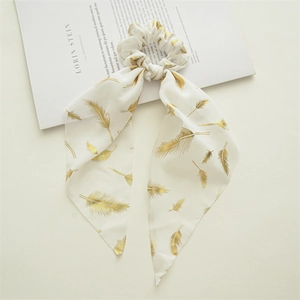 Detail of white chiffon scrunchie featuring golden feather prints and long ribbon ties