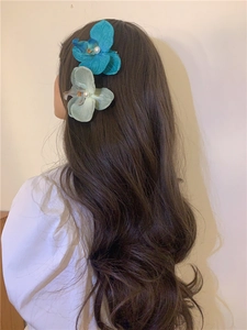 Detail of blue and green orchid hair clips with pearls on a model with long wavy hair