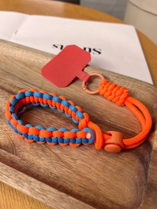 Close-up of woven paracord wrist strap with orange buckle and red phone patch on wood