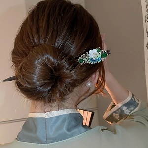 Detail view of a Chinese style hair pin with white flowers and green beads on an updo