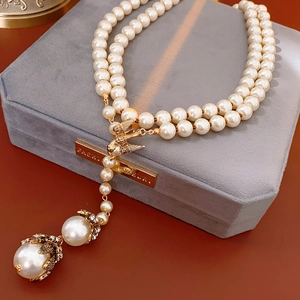 Detail view of double-layer pearl necklace with golden swallow and diamond flower charms