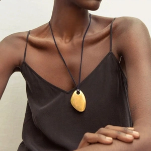 Detail of a minimalist gold pebble pendant on a black cord necklace worn by a model