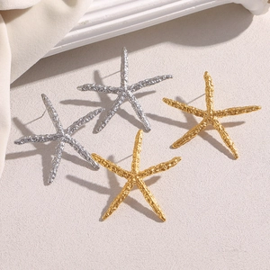 Dettaglio macro di orecchini a stella marina in oro 18K e argento con trama martellata