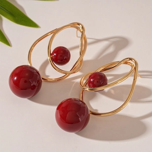 Detail of gold twisted wire earrings with red acrylic beads and silver pin accents