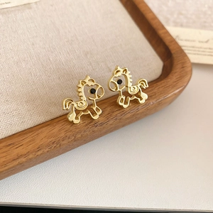 Macro shot of gold-plated hollow horse stud earrings on a wooden jewelry display tray