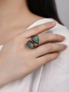 Close-up of a bronze adjustable ring with irregular green natural raw stones on a finger