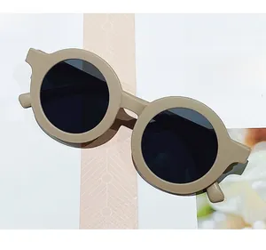 Detail view of round frame matte beige kids sunglasses on a magazine backdrop